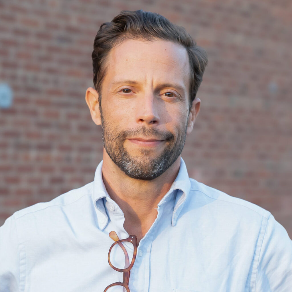 Individual in a light blue shirt standing against a brick wall.