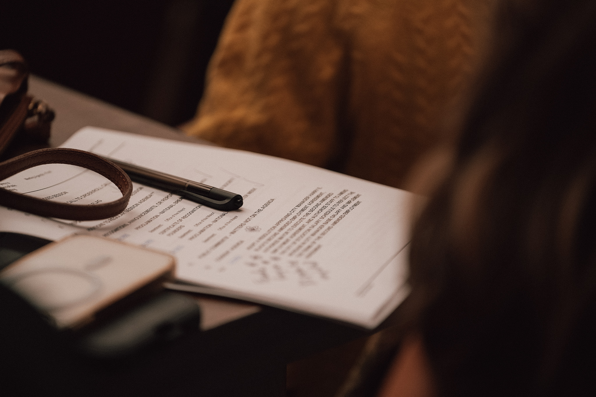 Close-up of a desk with a document, pen, and a leather strap.