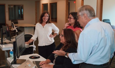 Four people interacting in a modern office around a desk with computers.